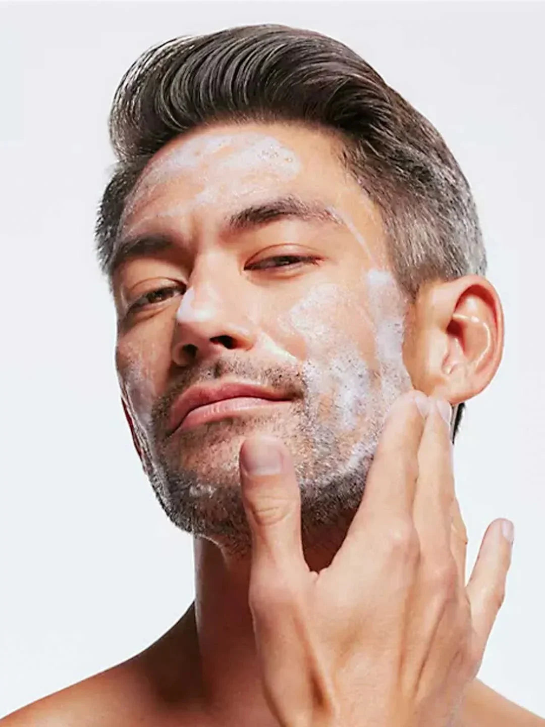 Man applying cream to his face with a neutral background