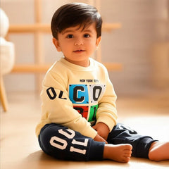 Child wearing a colorful sweater and navy pants with white text, sitting on a wooden floor.