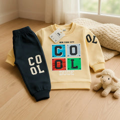 Children's yellow sweatshirt with colorful 'COOL' design and black pants on a wooden floor.