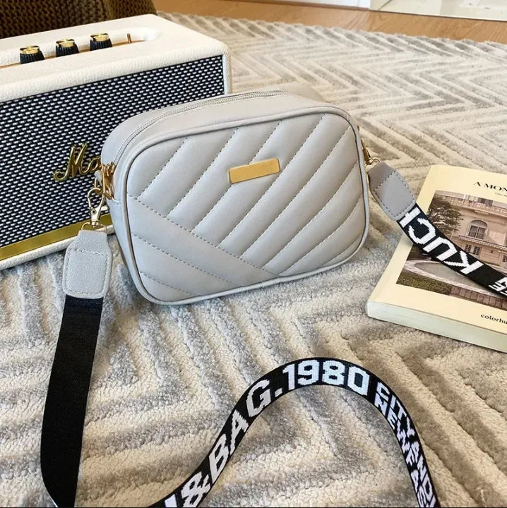 Gray quilted handbag with a black strap on a textured surface