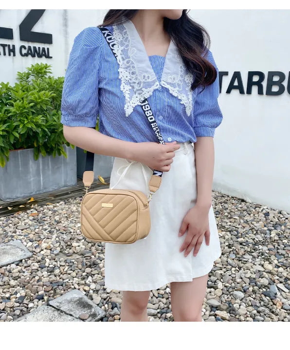 Person holding a beige quilted handbag in front of a white wall with branding.